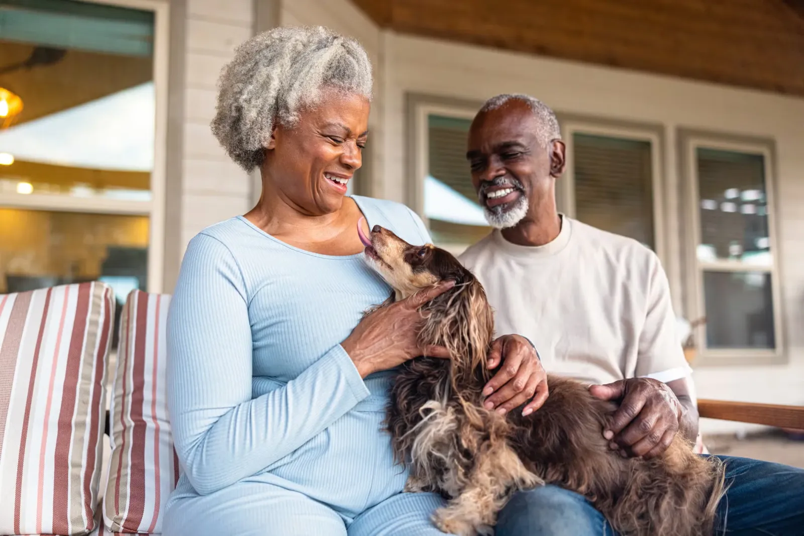A senior couple sitting on the porch with their Dachshund.
