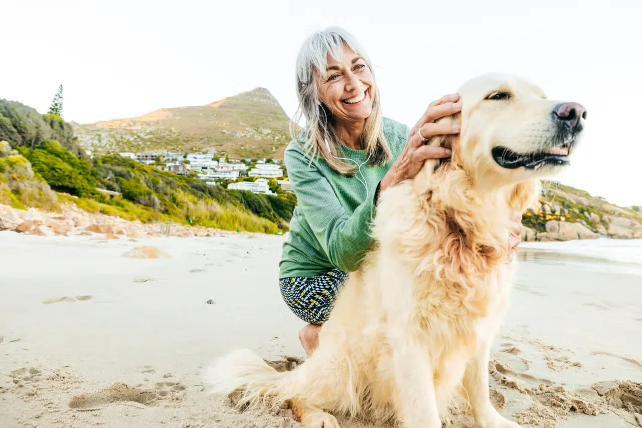 A senior woman playing with her Golden Retriever on a beach.